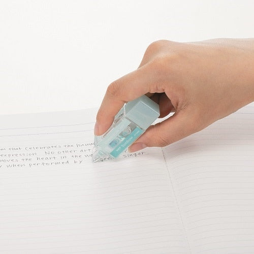 Tombow Mono Pocket correction tape in-use demonstration on lined notebook paper, showing blue tape dispenser held in hand