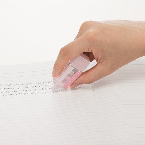 Mono Pocket correction tape in-use demonstration on notebook paper, pink tape dispenser held in hand
